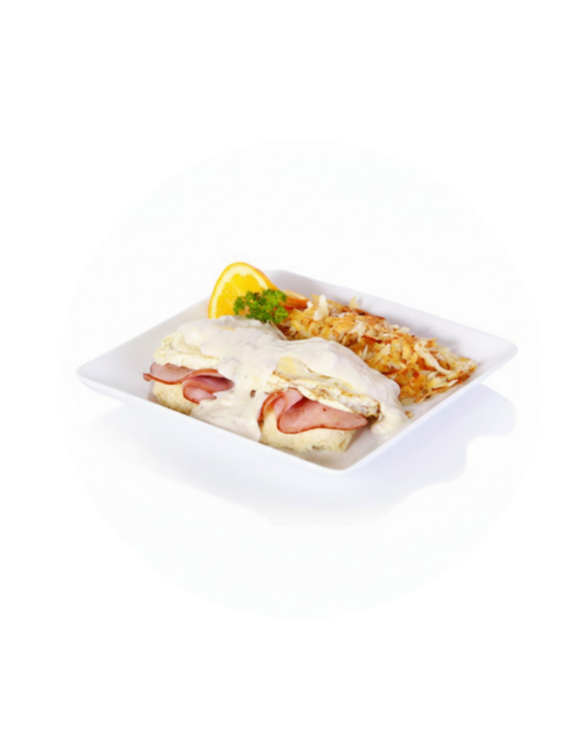 Plate with eggs benedict ham hollandaise and hash browns with an orange slice garnish on the side