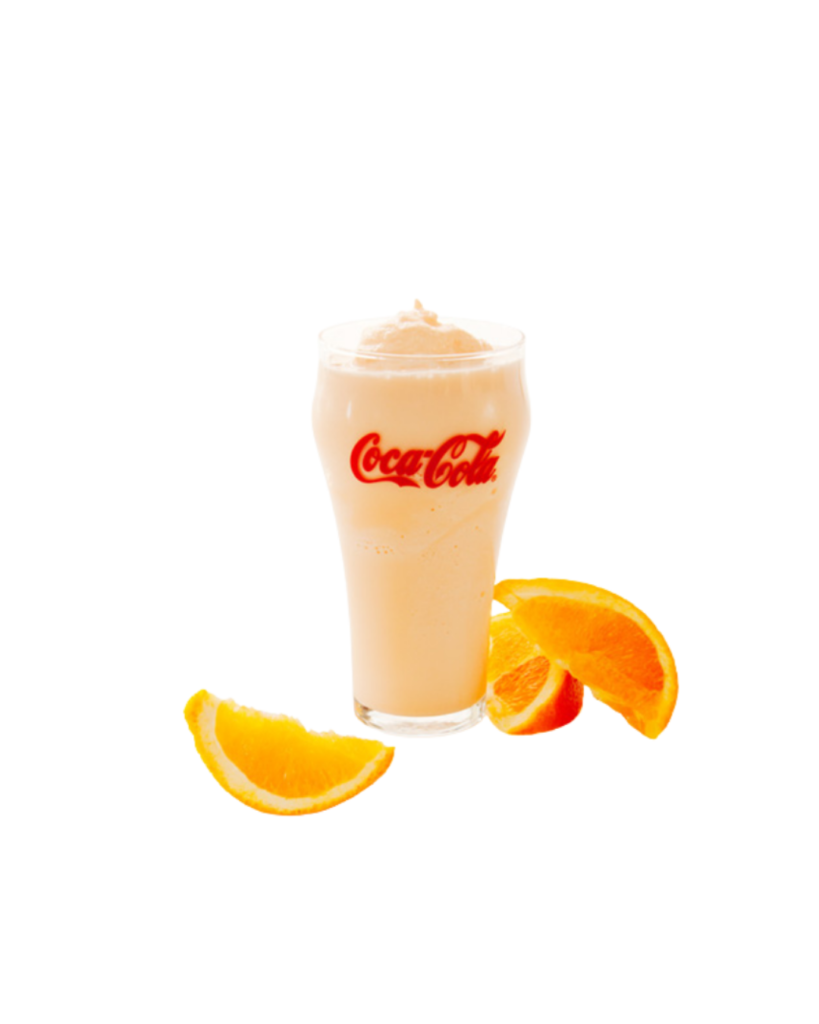Tall glass of orange coca cola with a foamy top logo visible surrounded by orange slices on a white background