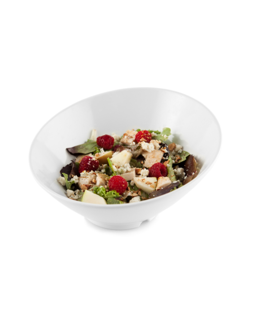 White bowl filled with mixed greens raspberries feta cheese and chopped nuts on a white background