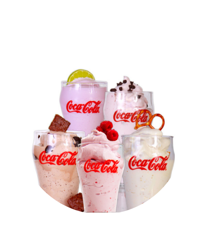 Assorted coca cola milkshakes in tall glasses topped with whipped cream and berries arranged together