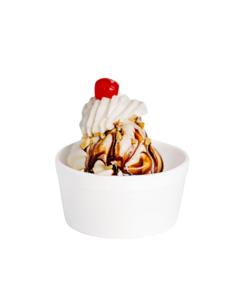 Vanilla soft serve in a white cup topped with whipped cream chocolate sauce chopped nuts and a cherry against a white background