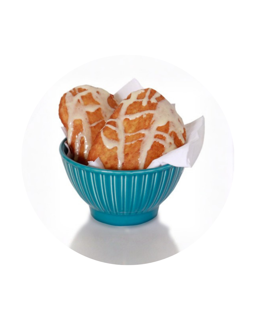 Two glazed muffins in a teal ribbed bowl lined with white paper napkins set against a white background